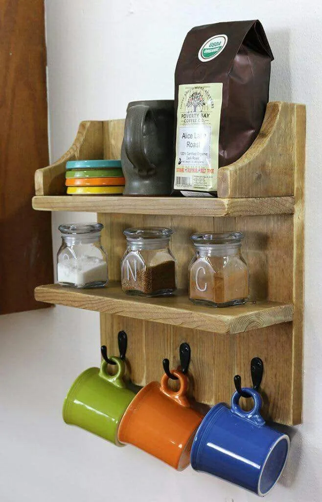 Estante de madera con ganchos negros de los que cuelgan tazas de colores y frascos