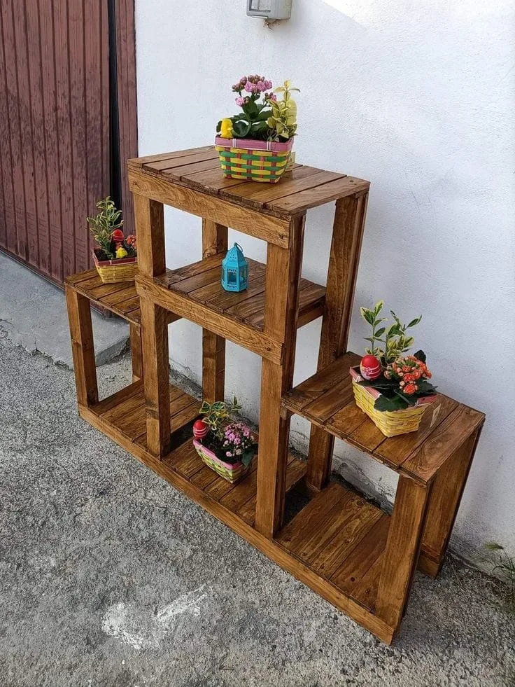 Estantes escalonados de madera con macetas de flores junto a una pared blanca