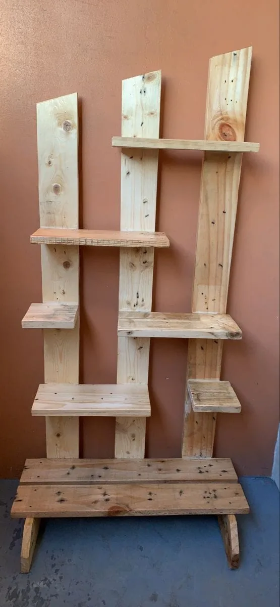 Estante alto de tablas claras con pequeños estantes salteados y un banquito en la base