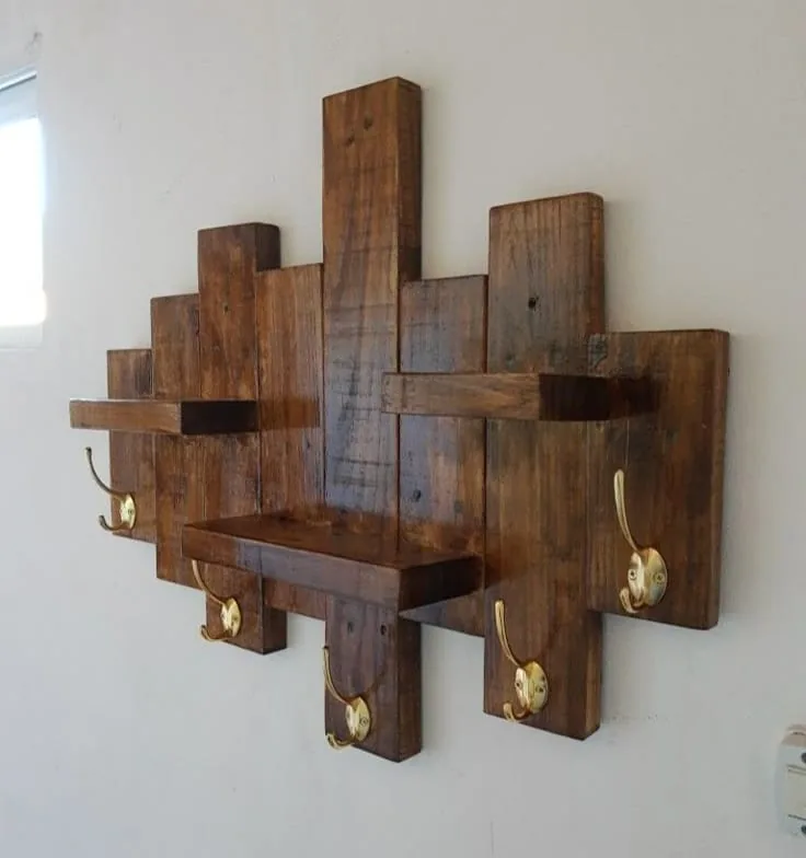 Perchero de pared armado con tablas oscuras a distintas alturas, con estantes y ganchos dorados